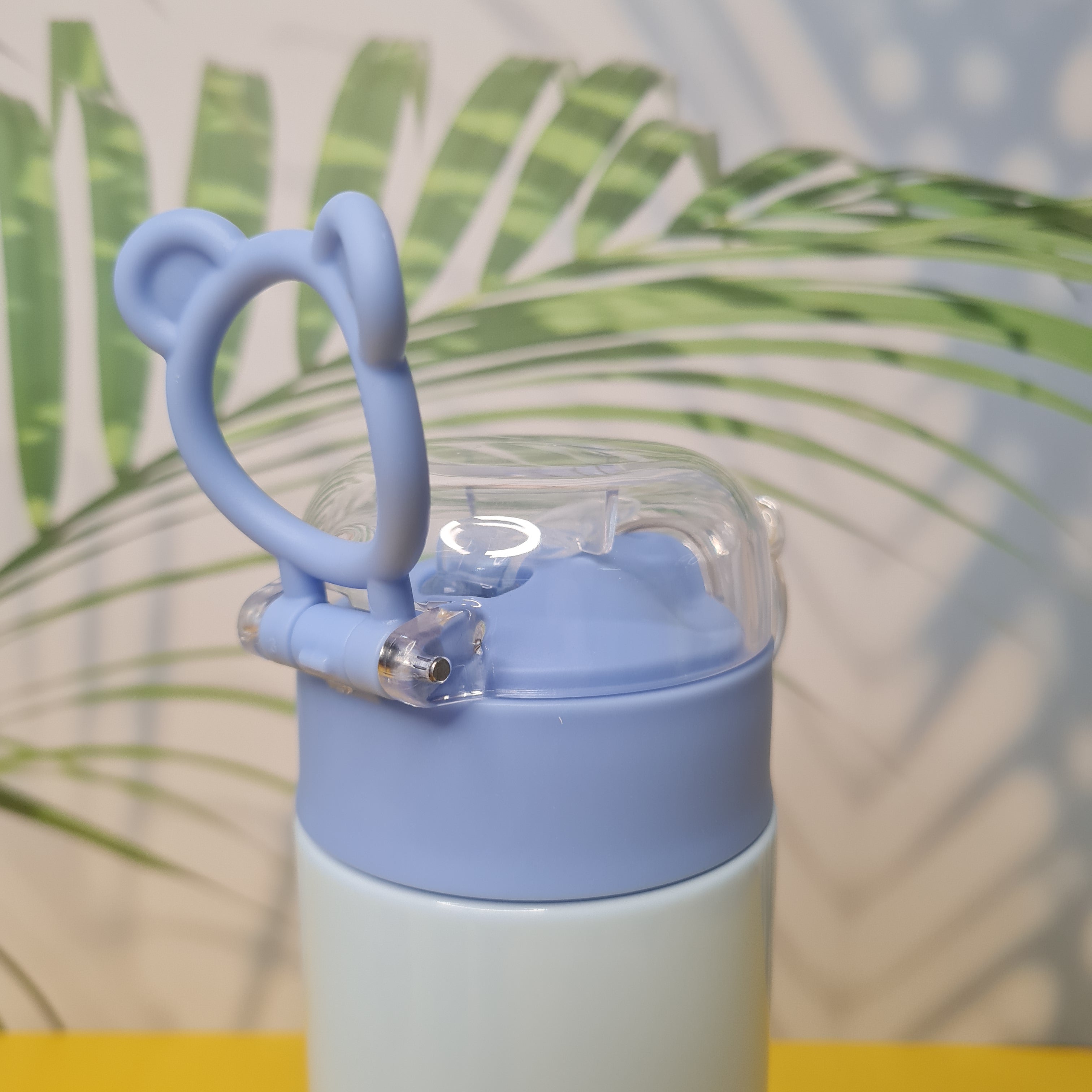 Baby bottle with blue handle against a blurred green leaf background